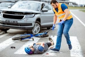 Man in orange safety vest rushes to help cyclist after collision with SUV near a crosswalk.