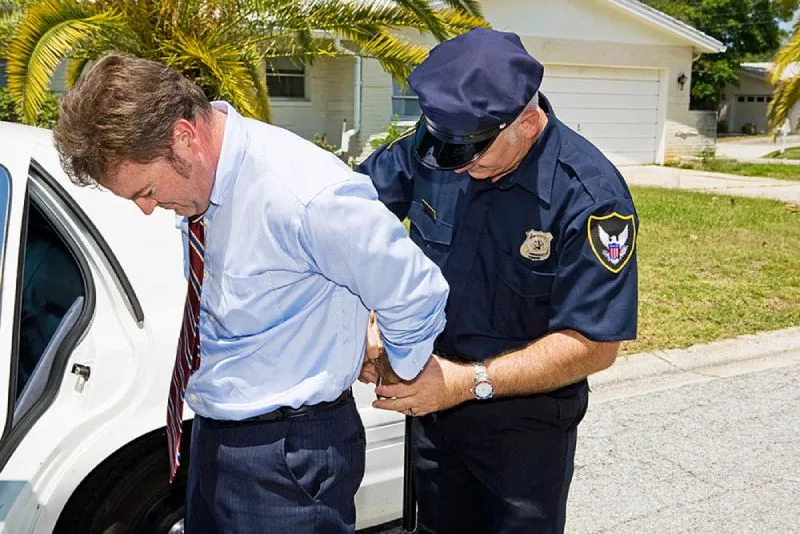 Officer places businessman in handcuffs in residential neighborhood.