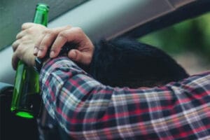 Close-up of a man's hands and arms holding a beer bottle while driving in West Michigan.