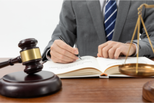 Personal injury lawyer writes in a book with a gavel and scales of justice in the foreground.