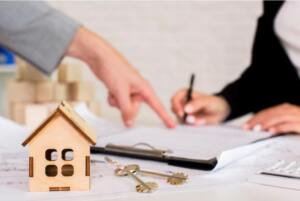 Woman points at signature line during a document signing with keys and model house in the foreground.