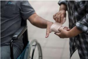 Woman wraps man's hand with an ACE bandage as he sits in a wheelchair.