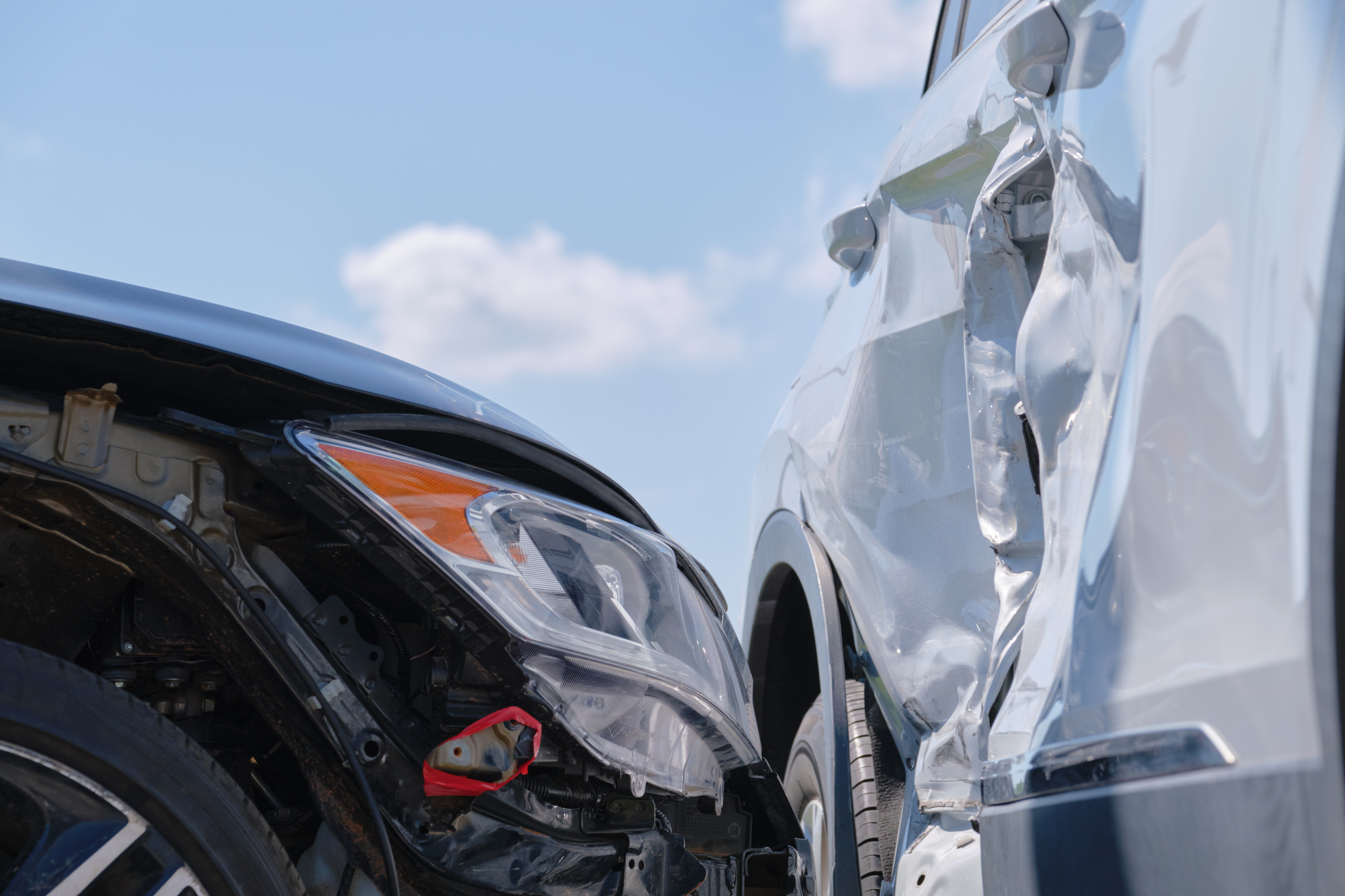 Close-up of two damaged vehicles after a collision, showing a crushed door and broken headlight.