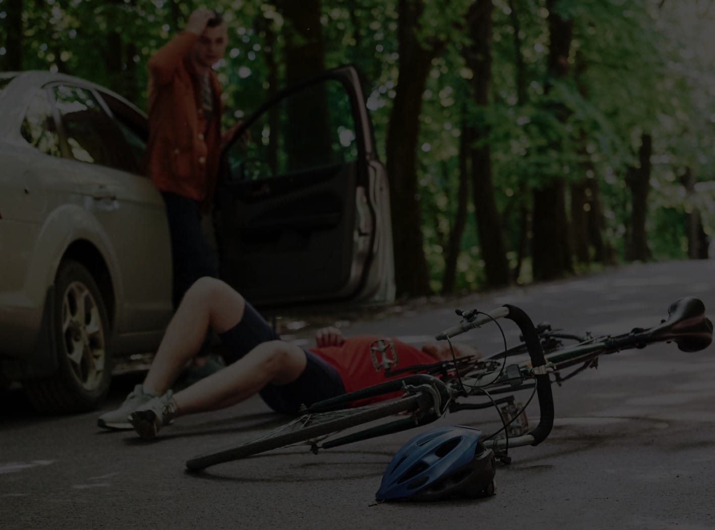 Cyclist lays on pavement near a bike as passenger steps out of car to check on crash victim.