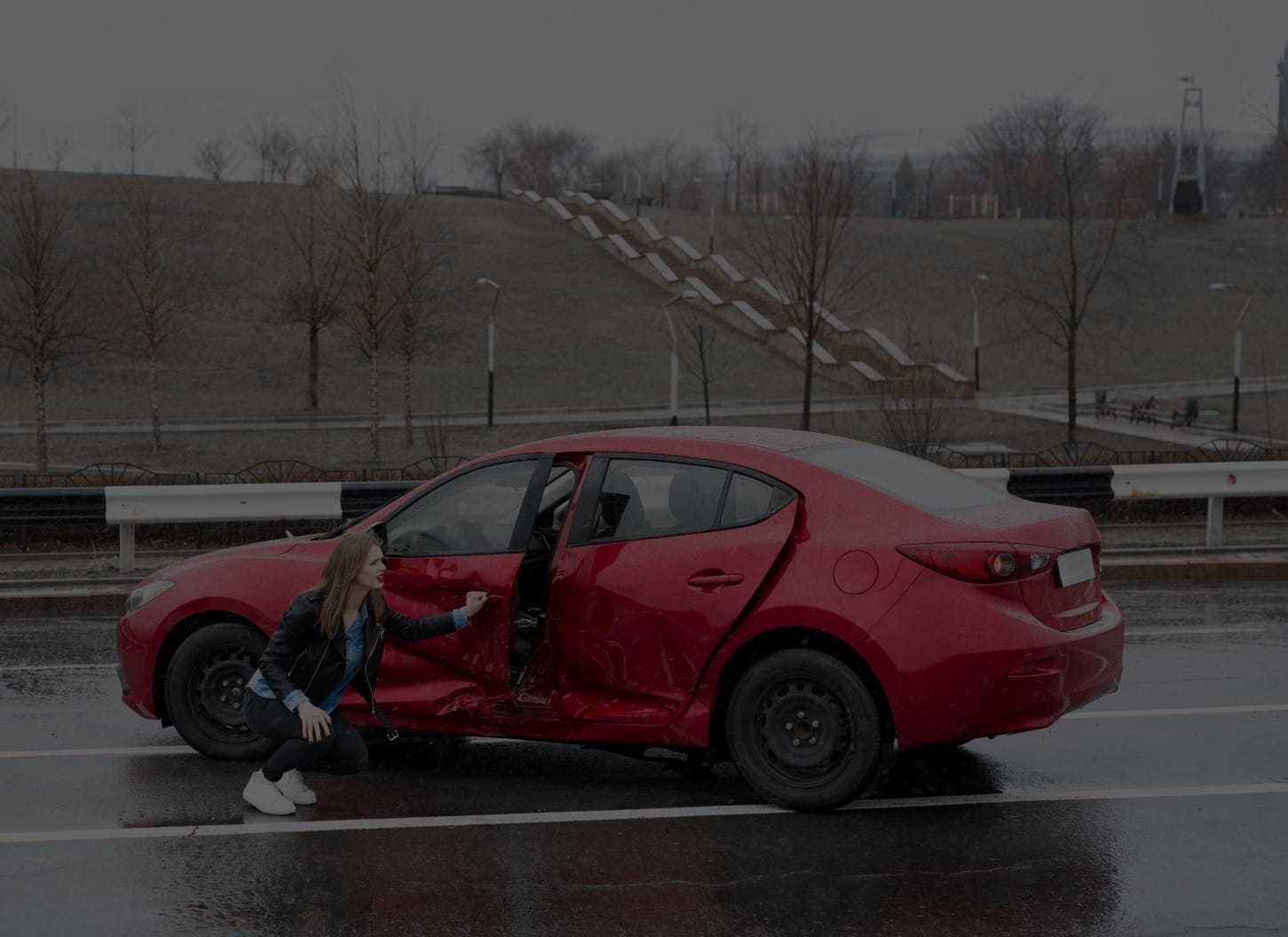 Woman crouches next to red sedan to check damage from T-bone collision.