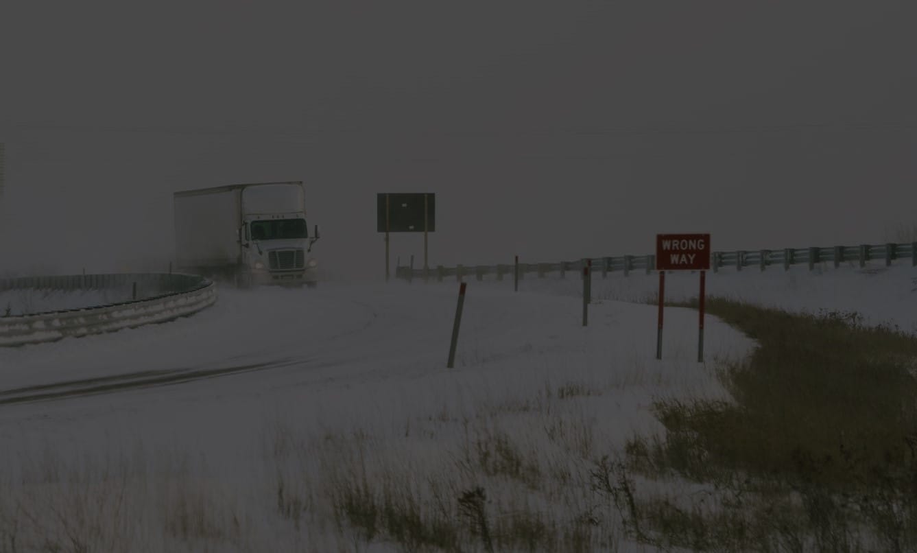 Tractor-trailer speeding down snow-covered highway exit ramp.