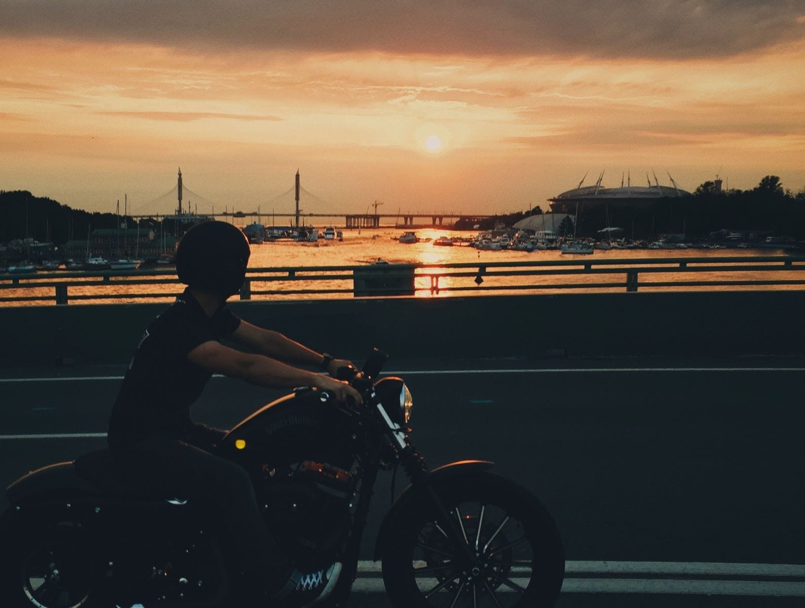 Motorcyclist drives over bridge in Grand Haven while looking over the water toward sunset.