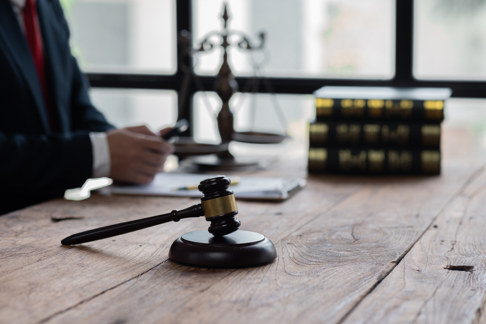 A lawyer sits at their desk that has a gavel, the scales of justice, and legal books on it.