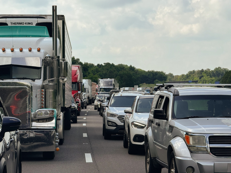 A semi truck, along with many other smaller vehicles, driving down the highway.