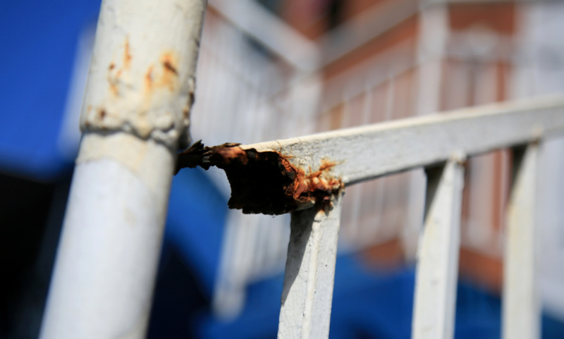 Close-up of a rusted and broken metal handrail on outdoor stairs.
