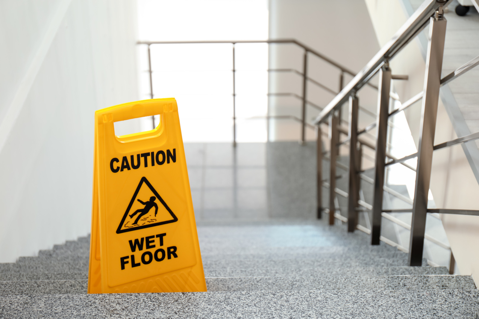 A wet floor sign on stairs with a metal railing.