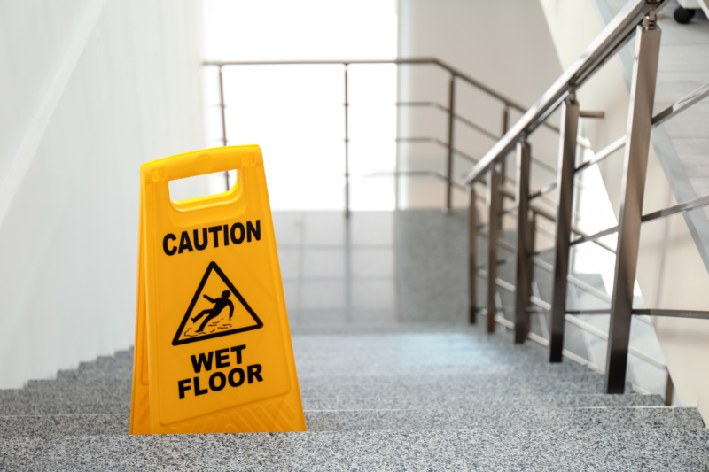 A wet floor sign on stairs with a metal railing.
